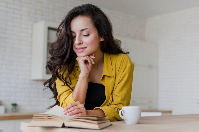 Mulher lendo um livro com um café na mesa