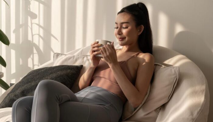 Mulher relaxando no sofá, segurando uma xícara.