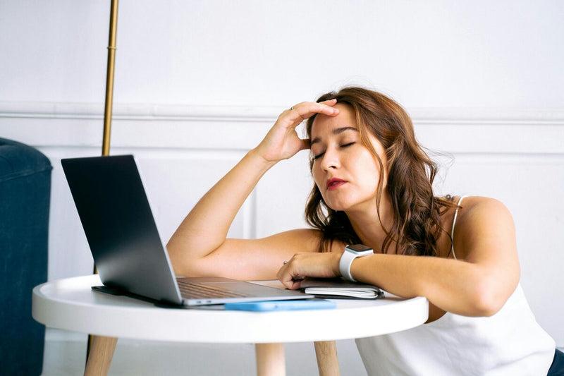 Mulher descansando com a mão na cabeça em frente ao laptop