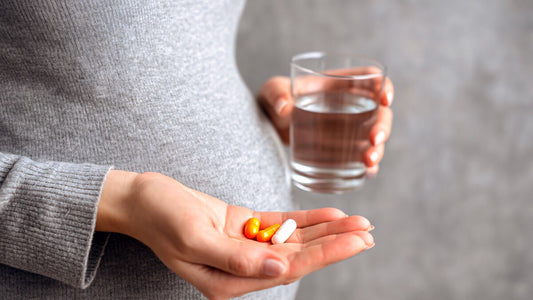 Mulher grávida segurando vitaminas e um copo d'água